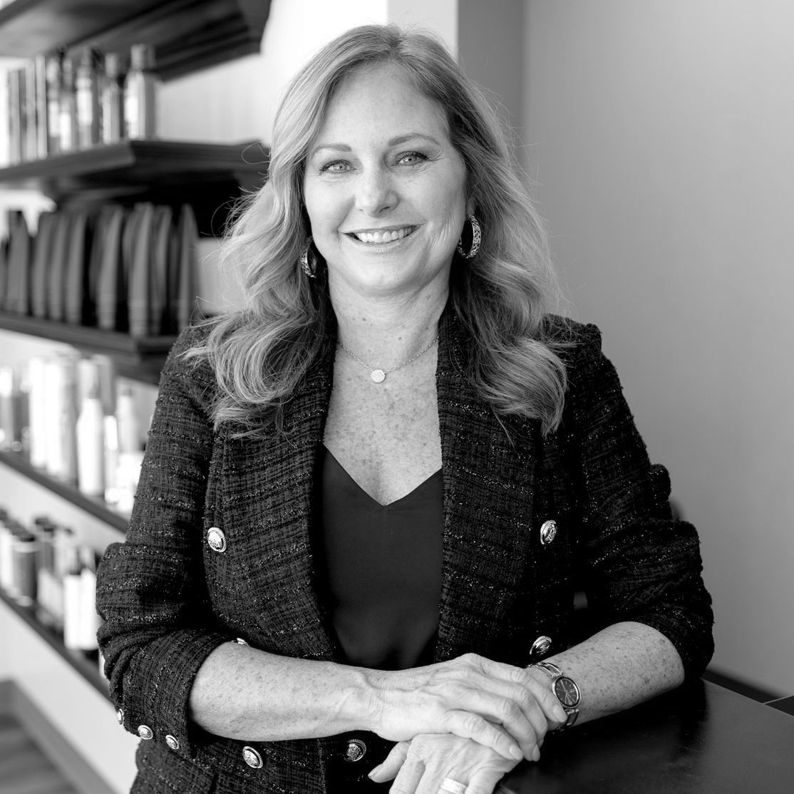 Black and White photo of a fair-skinned woman with loosely curled. She is wearing a blazer, jewlery, and minimal makeup.