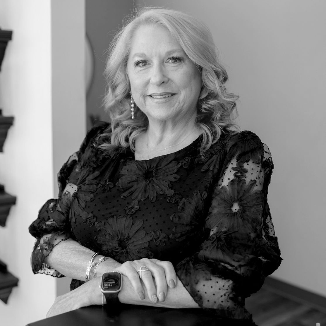 Black and White photo of a fair-skinned woman with light hair. She is wearing a top with sheer, puffy sleeves that is embroidered with black flowers.