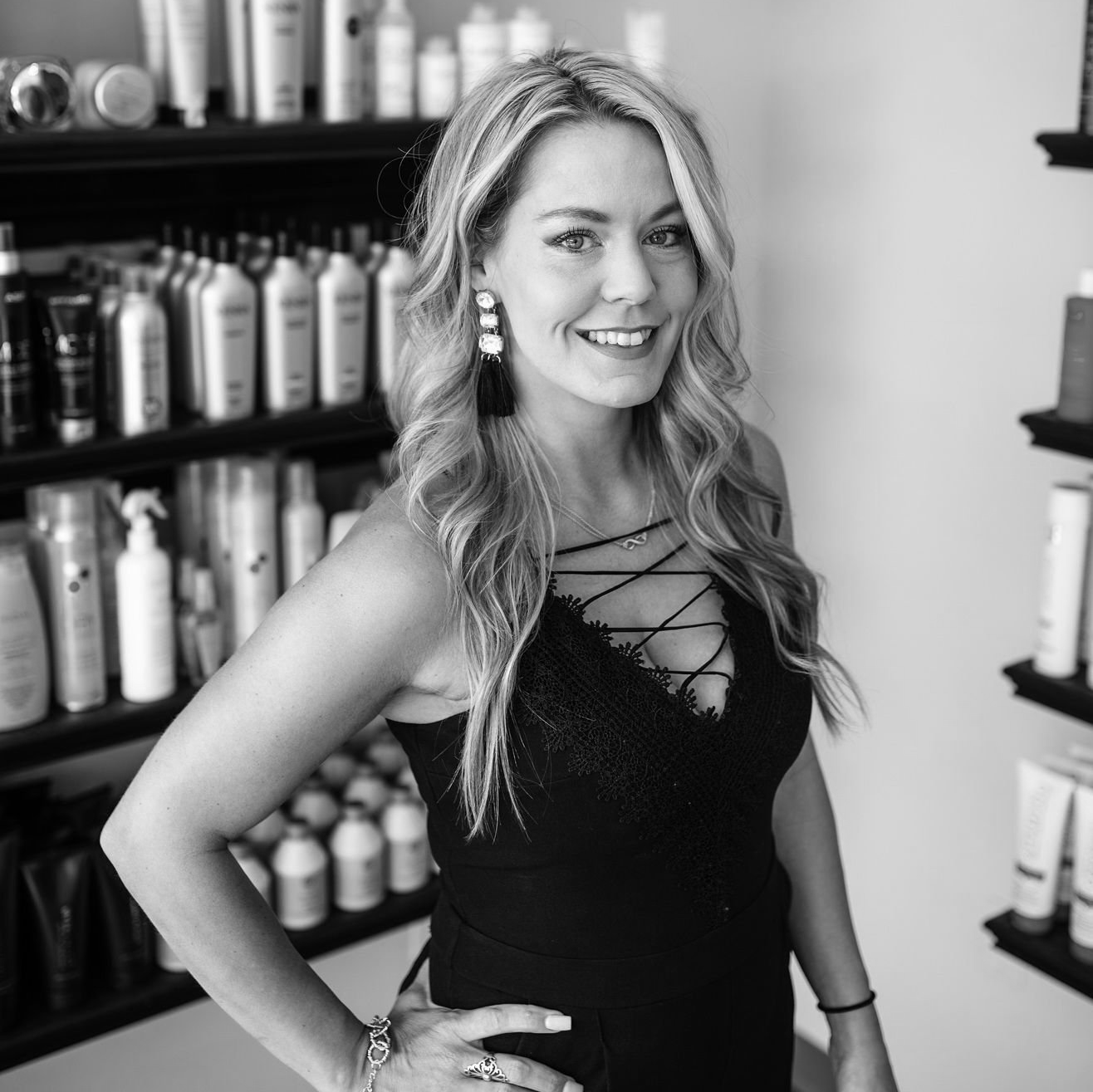 Black and White photo of a woman with long, light-colored curls. She is wearing a lacy dress with corset lacing across plunging v-neck along with a pair of large, bejewled earrings.
