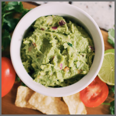 A bowl of guacamole with fresh tomatoes and lime around it.