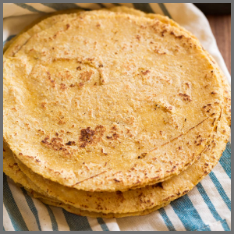 Lightly browned flour tortillas stacked atop a white and blue striped cloth.